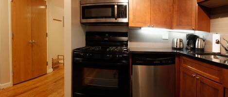 A kitchen with wooden cabinets, a stainless steel microwave, a black stove, and a dishwasher.