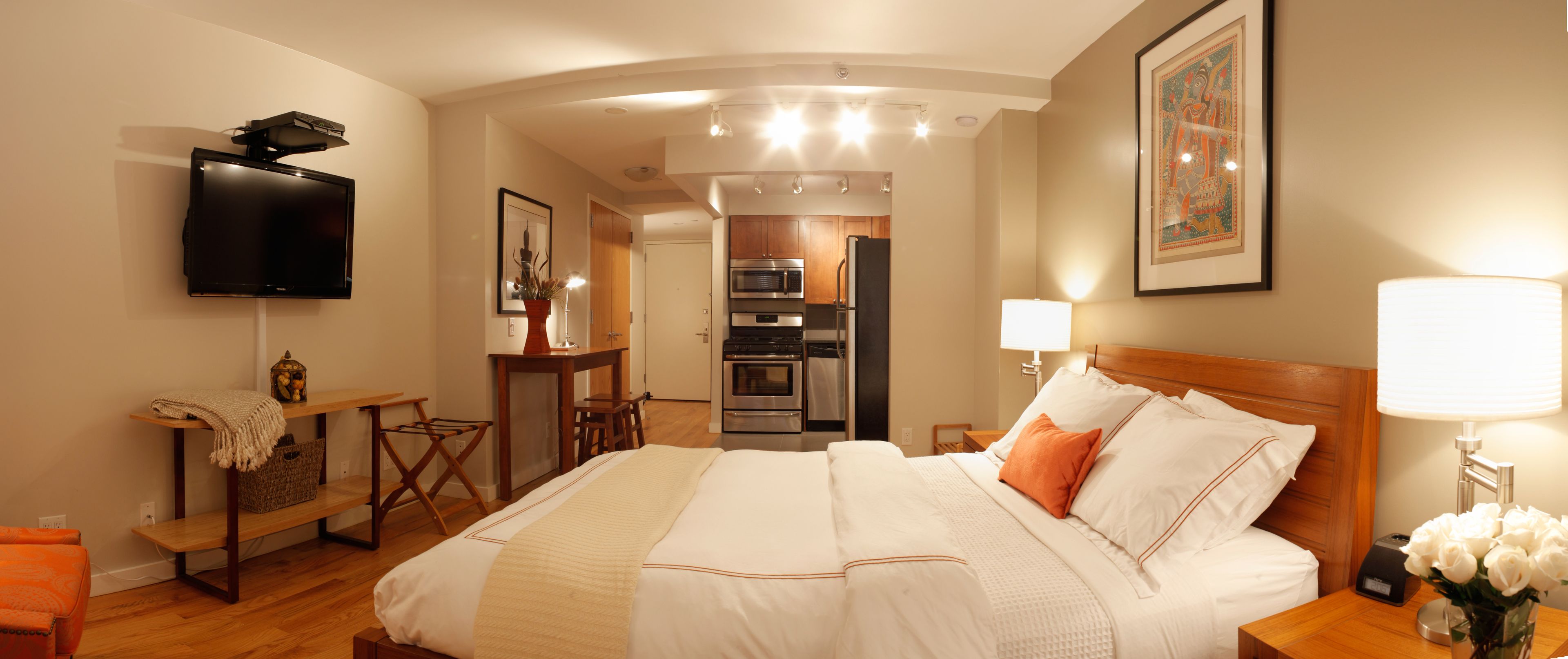 A hotel room with a bed, a TV, a desk, a lamp, and a picture on the wall.