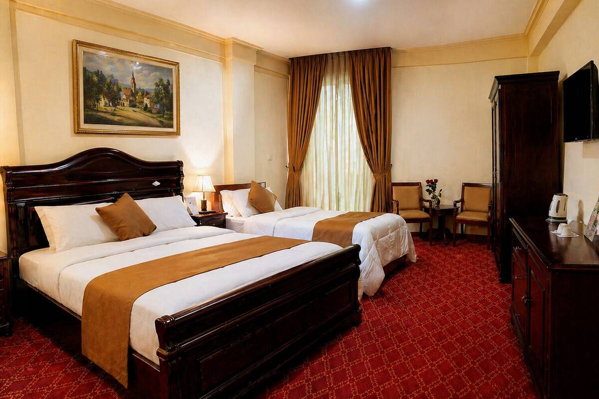 Quarto de hotel com duas camas, um quadro na parede, uma mesa com cadeira e uma televisão.