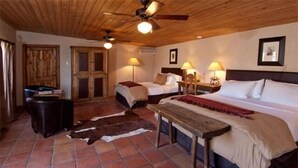 Habitación con dos camas, un ventilador de techo de madera y una decoración rústica que incluye una silla de montar de cuero y un banco de madera.