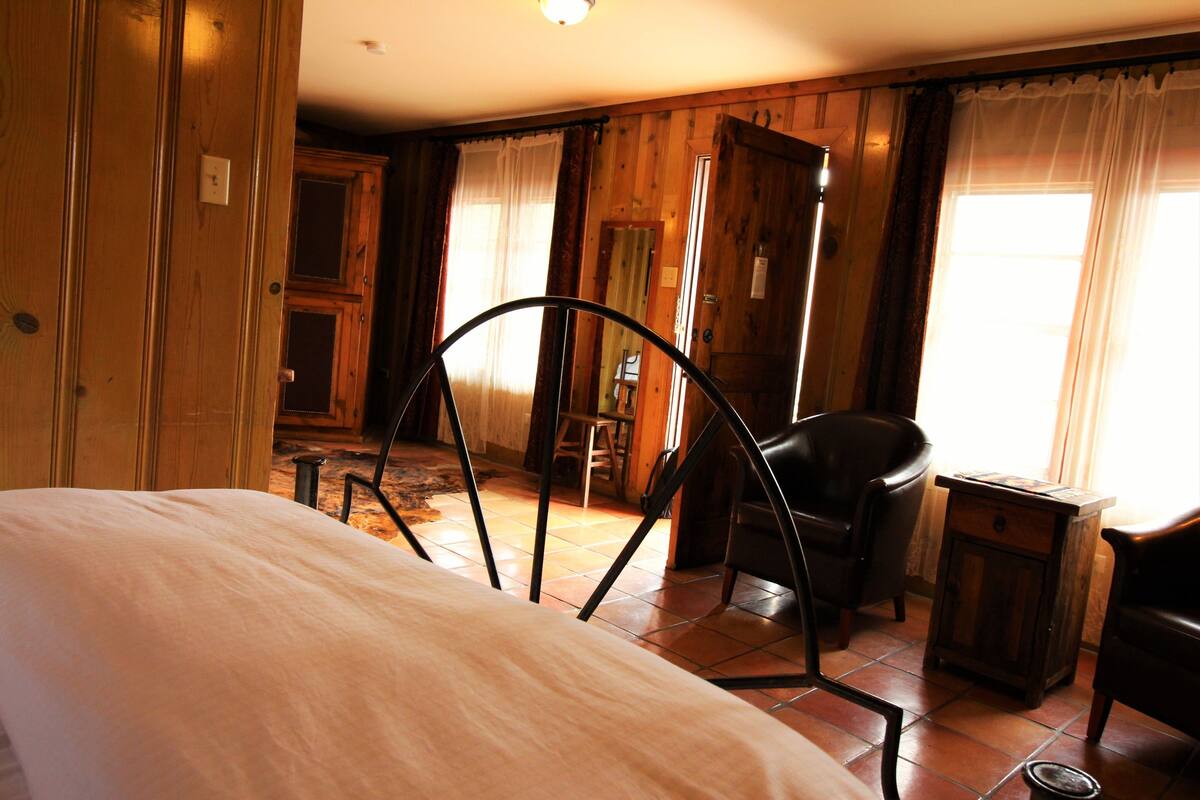 A room with a bed, a chair, a small table, and a wooden wardrobe.