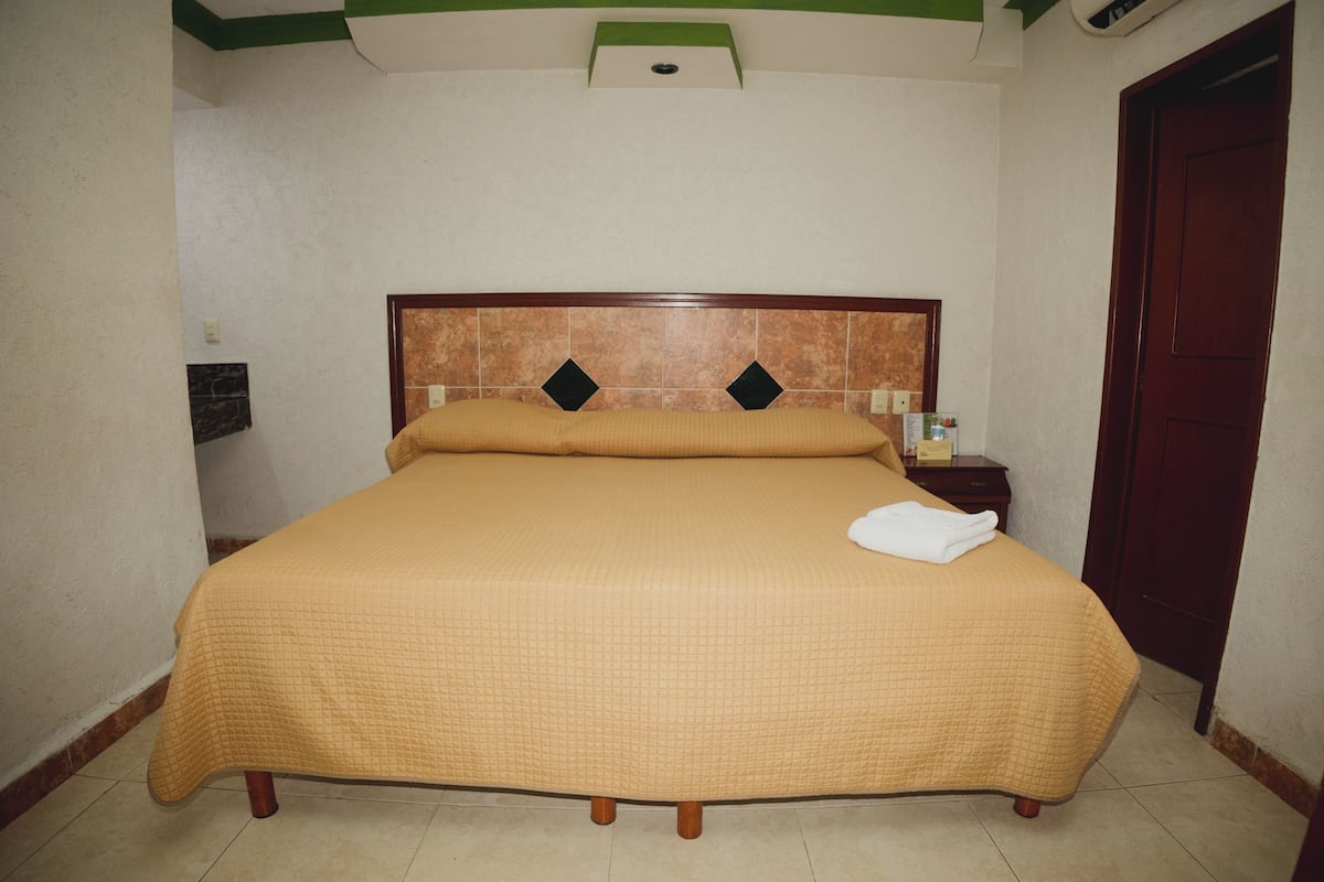 A bed with a quilted cover, a wooden headboard with diamond-shaped decorations, a nightstand with a lamp, and a door to the right.