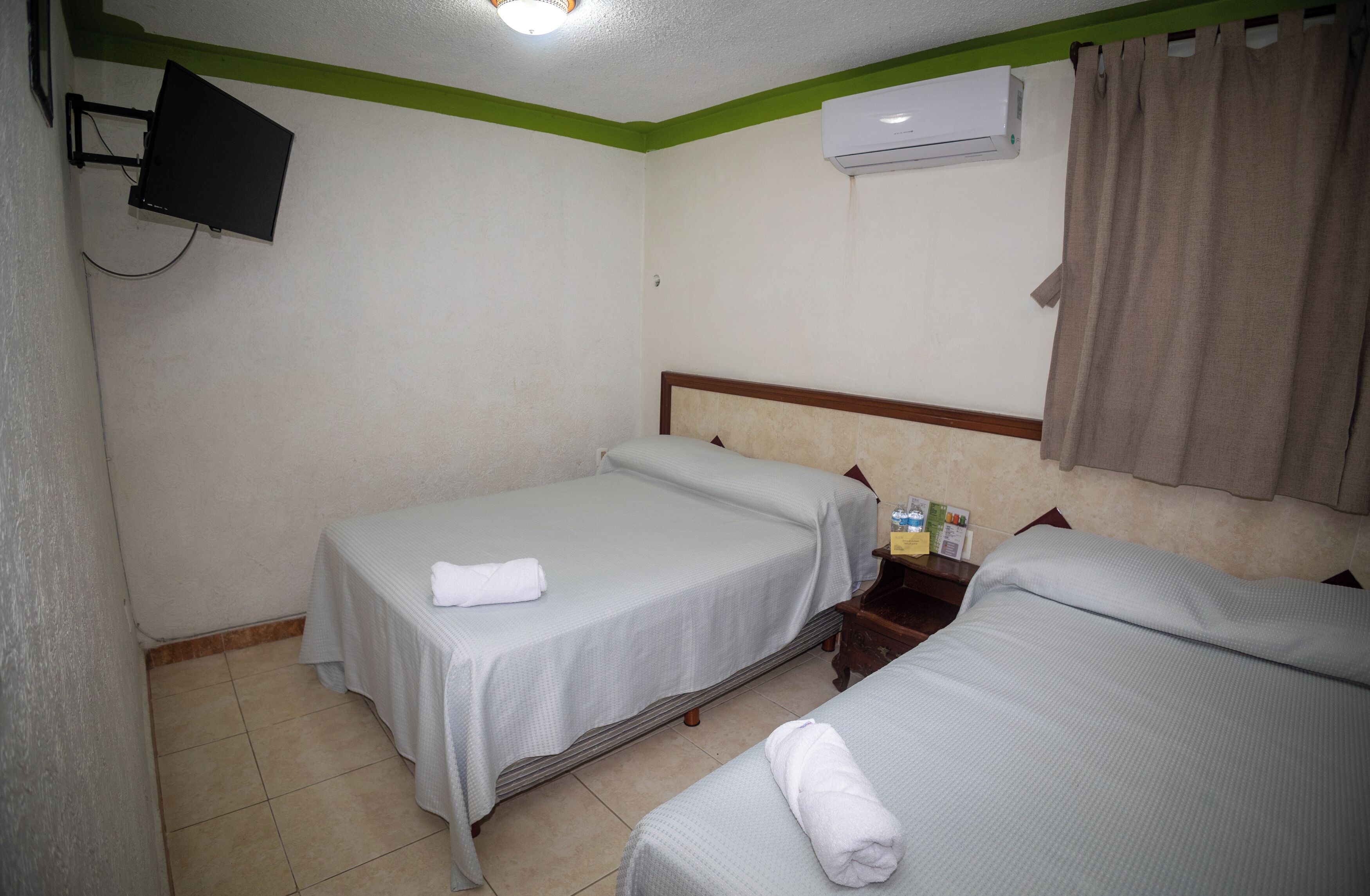 Una habitación de hotel con dos camas, un televisor montado en la pared, un equipo de aire acondicionado y una cortina.