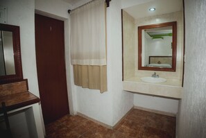 A bathroom with a wooden door, a beige curtain, a sink with a mirror, and brown tiled flooring. - Nicte Ha Campeche (Campeche)