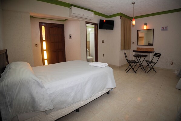 A hotel room with a bed, a desk with chairs, a TV, and a mirror.