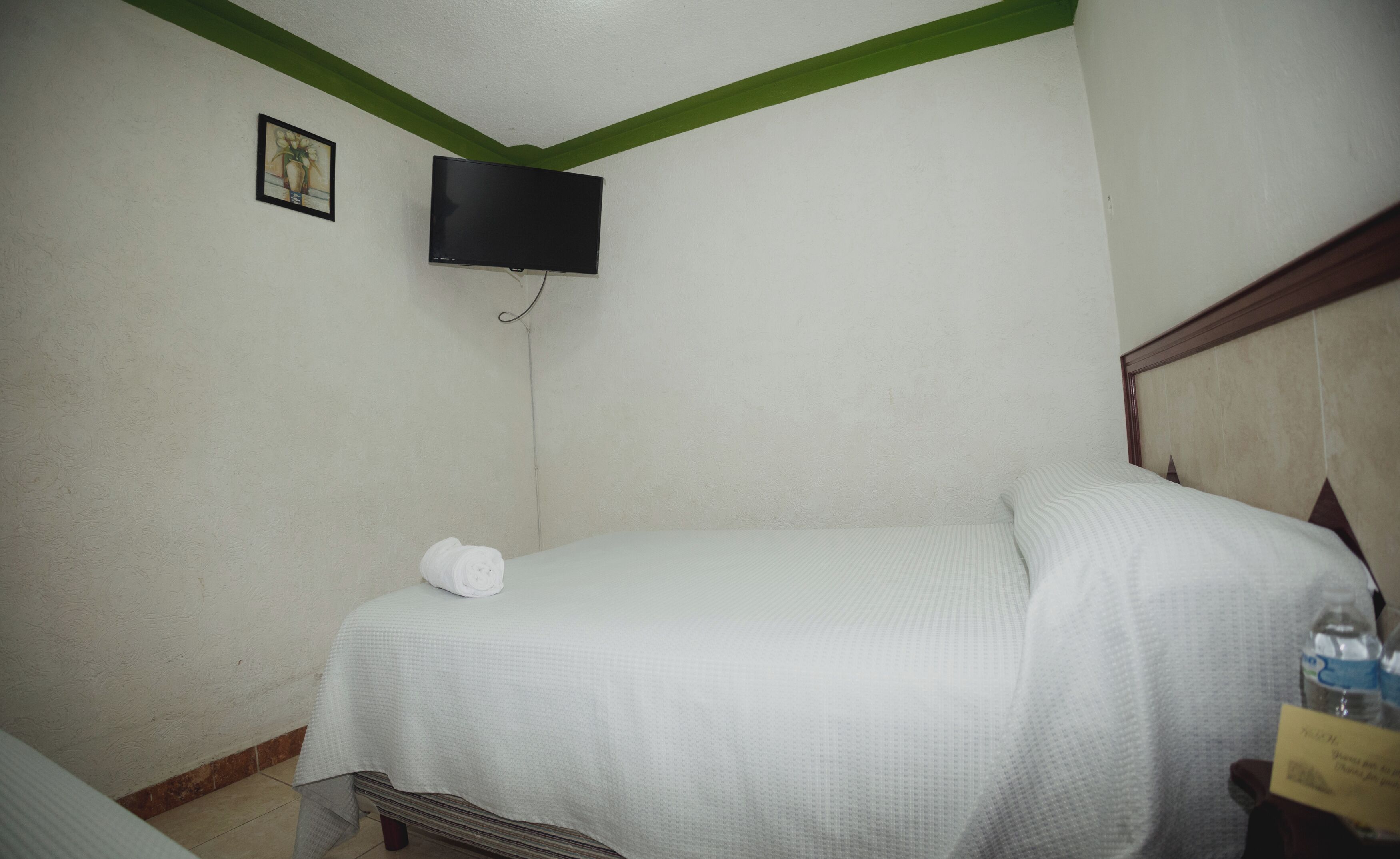 Une petite pièce simple, avec un lit, un téléviseur fixé au mur et un petit cadre photo.