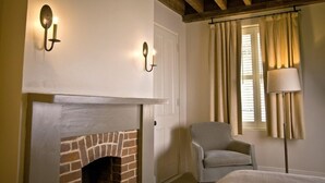 Une pièce avec une cheminée en briques, deux appliques murales, un fauteuil gris, une table de chevet et un lampadaire.