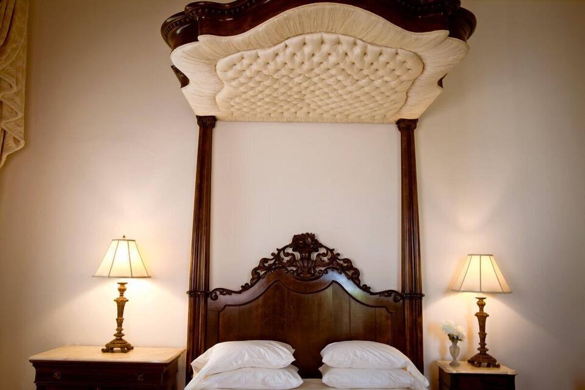 A four-poster bed with a high, ornate headboard, flanked by two bedside tables with lamps.
