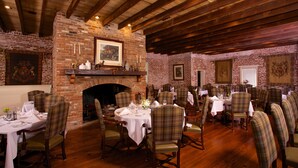 Un restaurant aux murs de briques, aux poutres en bois et aux chaises à carreaux. Les tables sont dressées avec des nappes blanches et de beaux couverts.