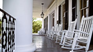 Une véranda avec des fauteuils à bascule blancs et une balustrade en fer forgé noir.