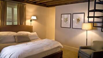 A bedroom with a large bed, a chair, a lamp, and framed botanical prints on the wall.