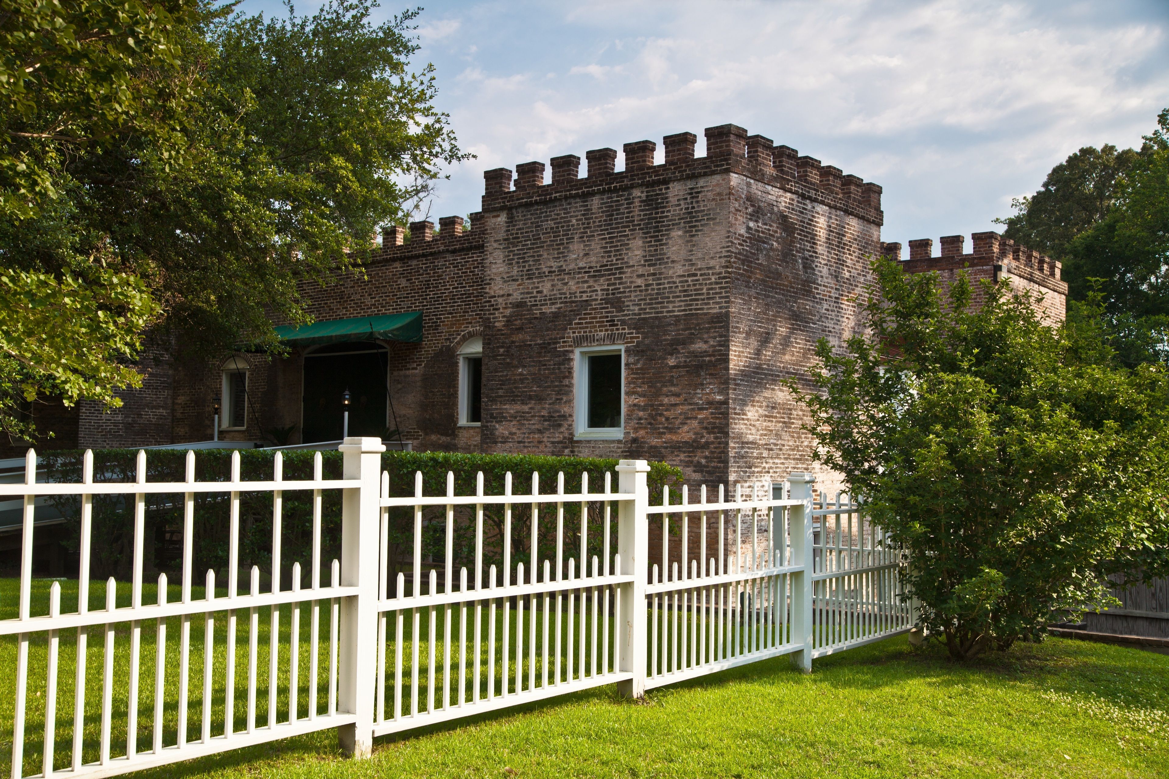 A brick building with a white picket fence in front, surrounded by greenery.