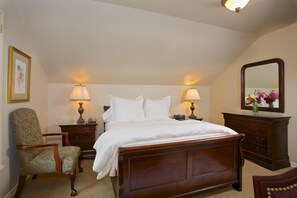 A neatly arranged bedroom with a large bed, two bedside tables with lamps, a chair, a dresser, and a mirror on the wall.