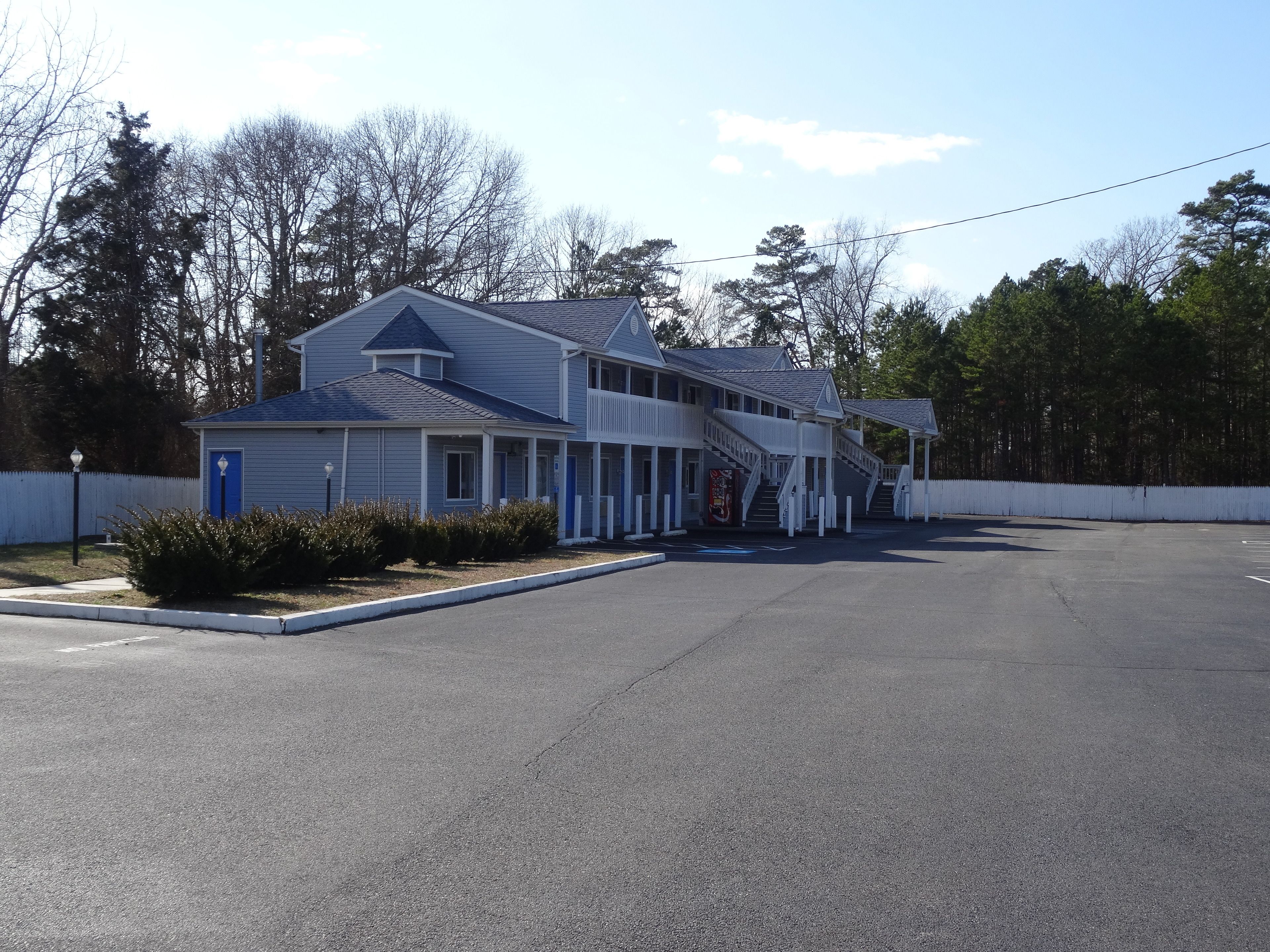 A motel with a central building and two attached wings, featuring a covered walkway and a parking lot.