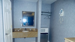 A bathroom with a sink, mirror, hairdryer, and a small refrigerator. - Village Inn and Suites (Absecon)