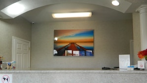 A reception desk with a painting of a sunset over a bridge, a white door, and a no smoking sign. - Village Inn and Suites (Absecon)