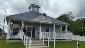 A two-story building with a porch, a small tower-like structure on the roof, and a flag on the flagpole. - Village Inn and Suites (Absecon)