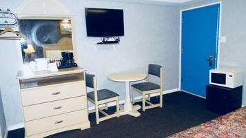 A hotel room with a bed, a desk with a chair, a television, and a blue door.