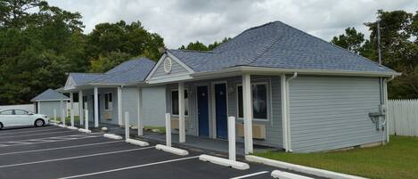 Une rangée de petits bâtiments d’un seul étage, typiques des motels, au design simple et fonctionnel, avec un espace de stationnement couvert à l’avant.