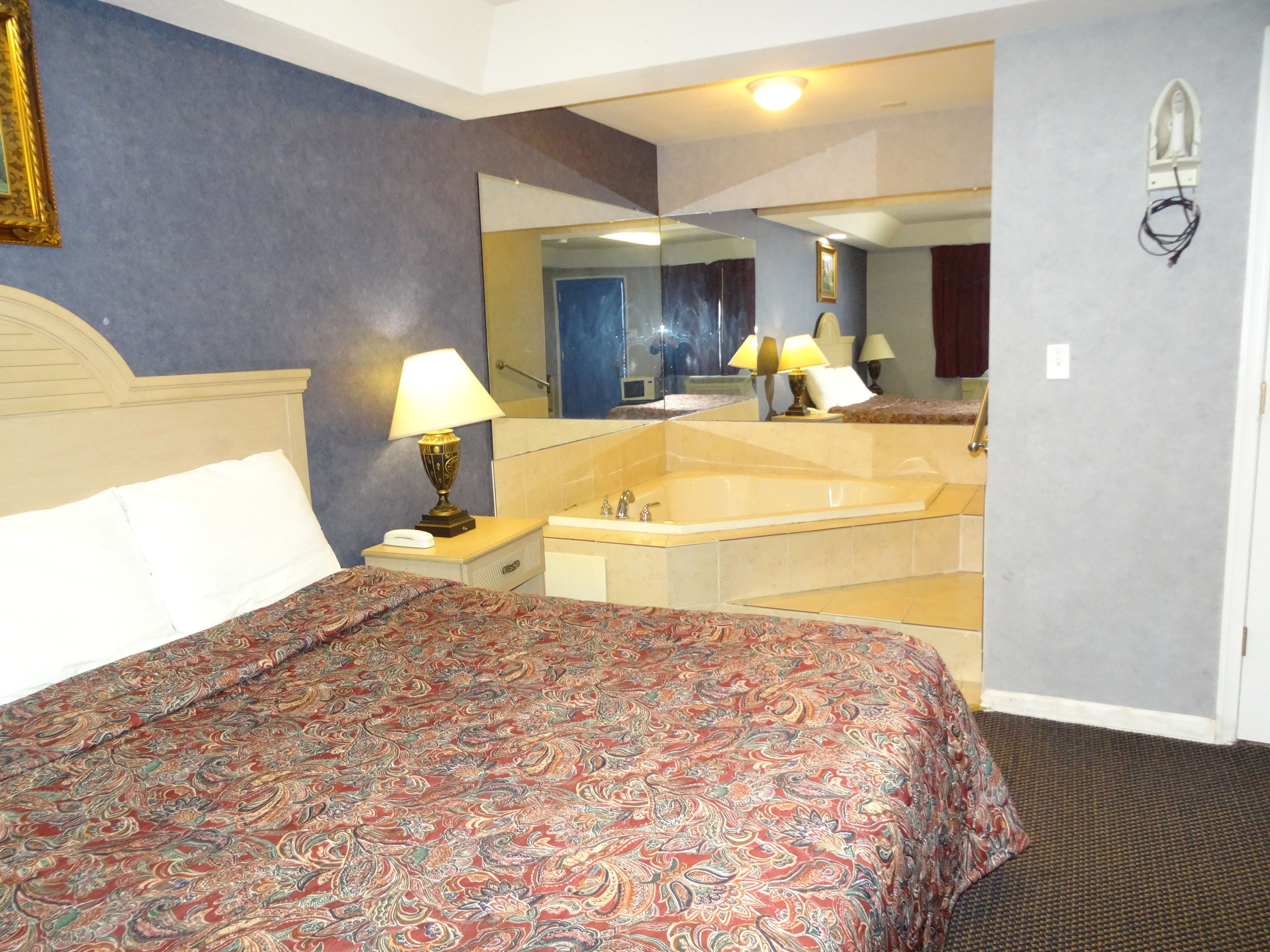 Une chambre d’hôtel avec un grand lit, un coin salon avec une lampe, une baignoire et un grand miroir.