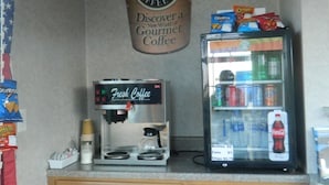 A coffee station with a coffee machine, a refrigerator stocked with beverages, and a sign advertising gourmet coffee. - Village Inn and Suites (Absecon)