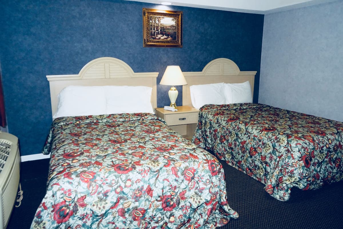 A hotel room with two beds, a nightstand with a lamp, a framed picture on the wall, and a telephone on the left.