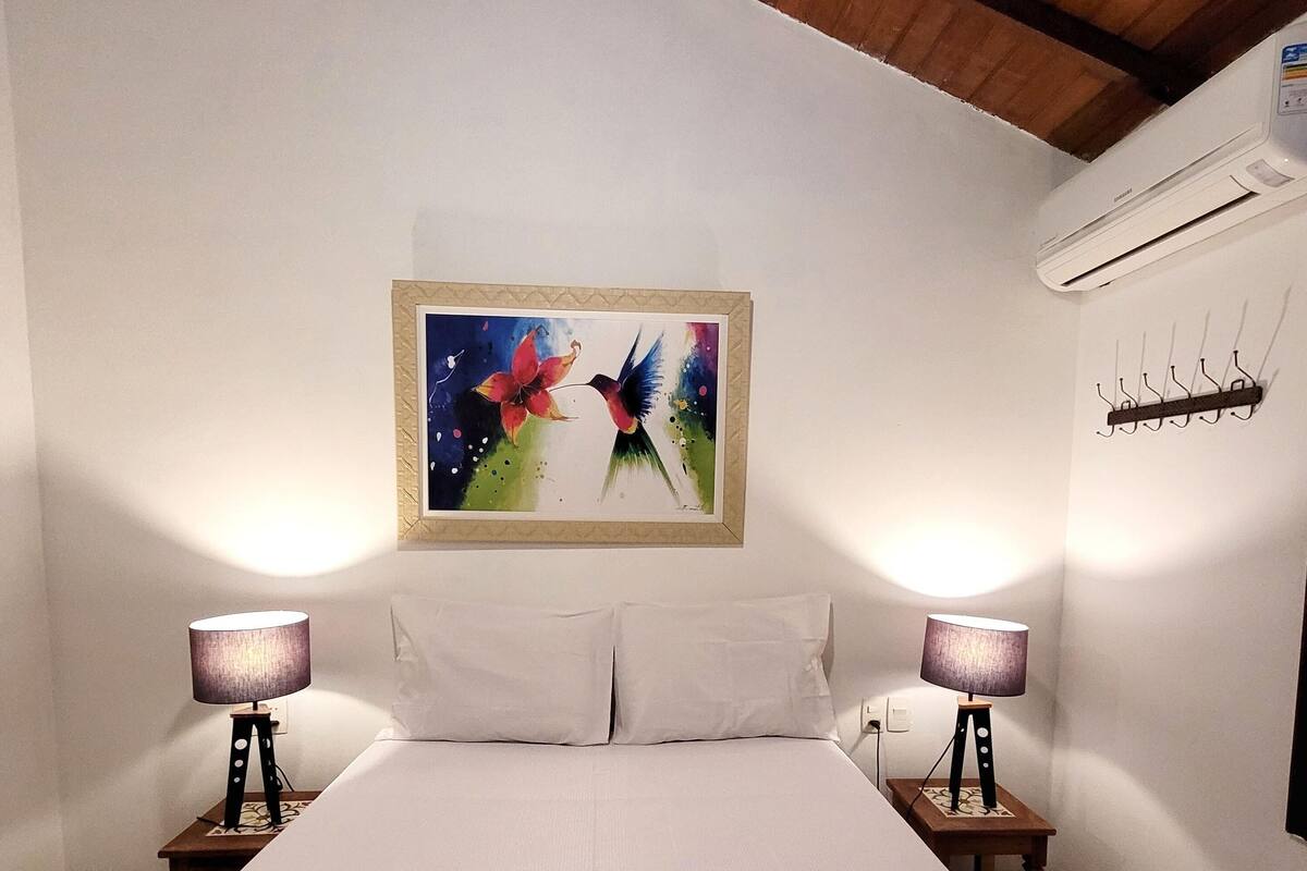 Une chambre d’hôtel avec un grand lit, deux lampes de chevet, un tableau au mur et une serviette avec des articles de toilette posée sur le lit.