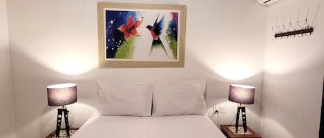 A hotel room with a large bed, two bedside lamps, a painting on the wall, and a towel with toiletries on the bed.