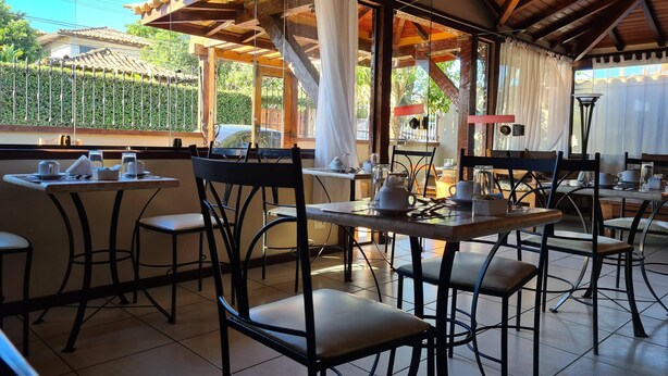 Een terras met tafels en stoelen, een houten plafond en uitzicht op groen en een hek.