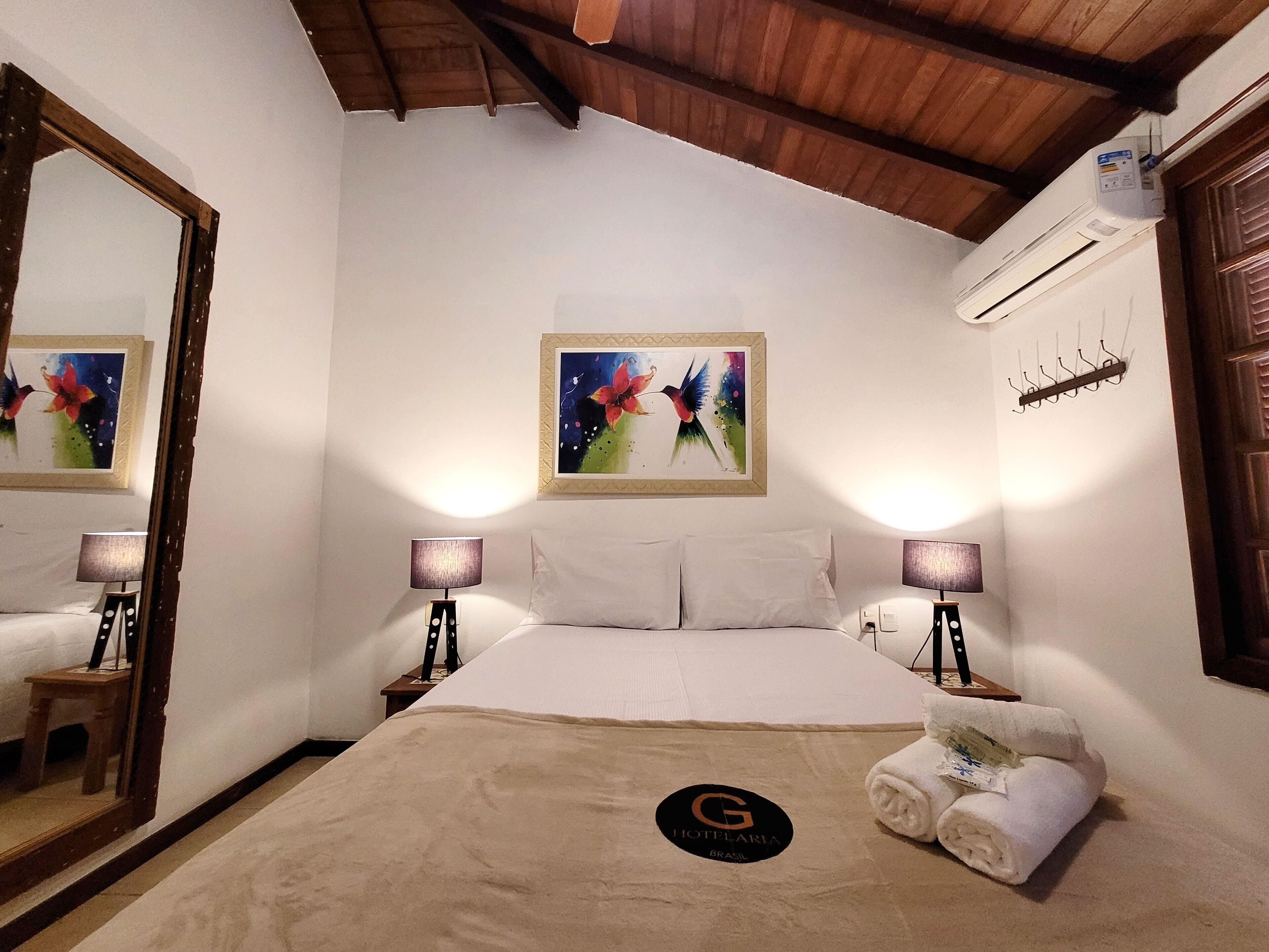 Une chambre d’hôtel avec un lit, deux lampes de chevet, un tableau au mur, un porte-serviettes et un panneau sur le lit.