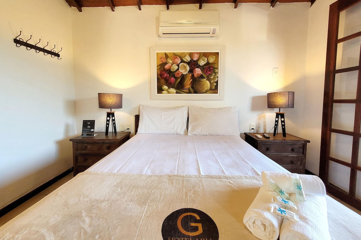 Une chambre d’hôtel avec un lit, deux tables de chevet, un tableau, un climatiseur et une serviette ornée d’un logo.
