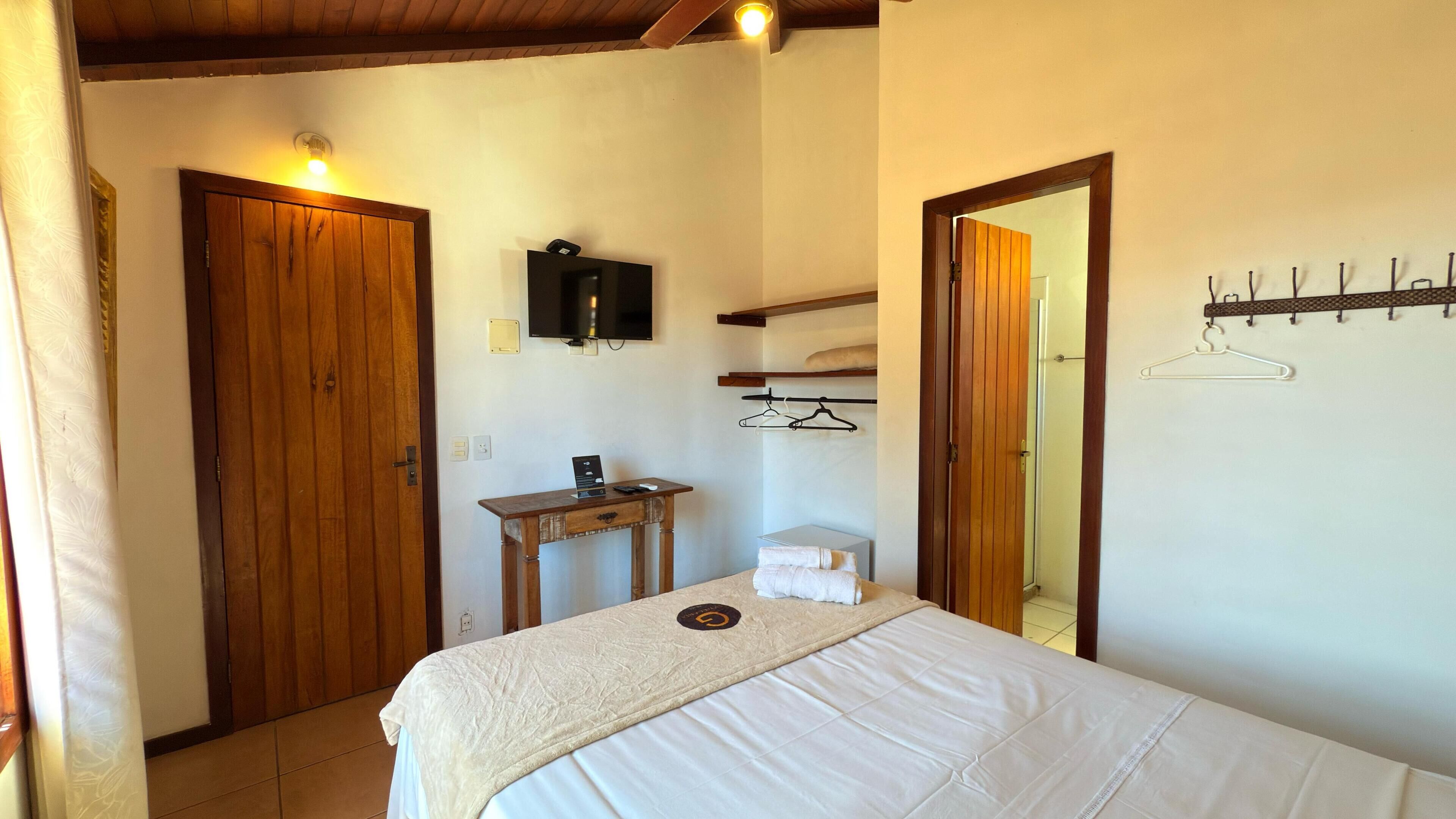 A bedroom with a bed, a wooden desk, a television, and a coat rack.