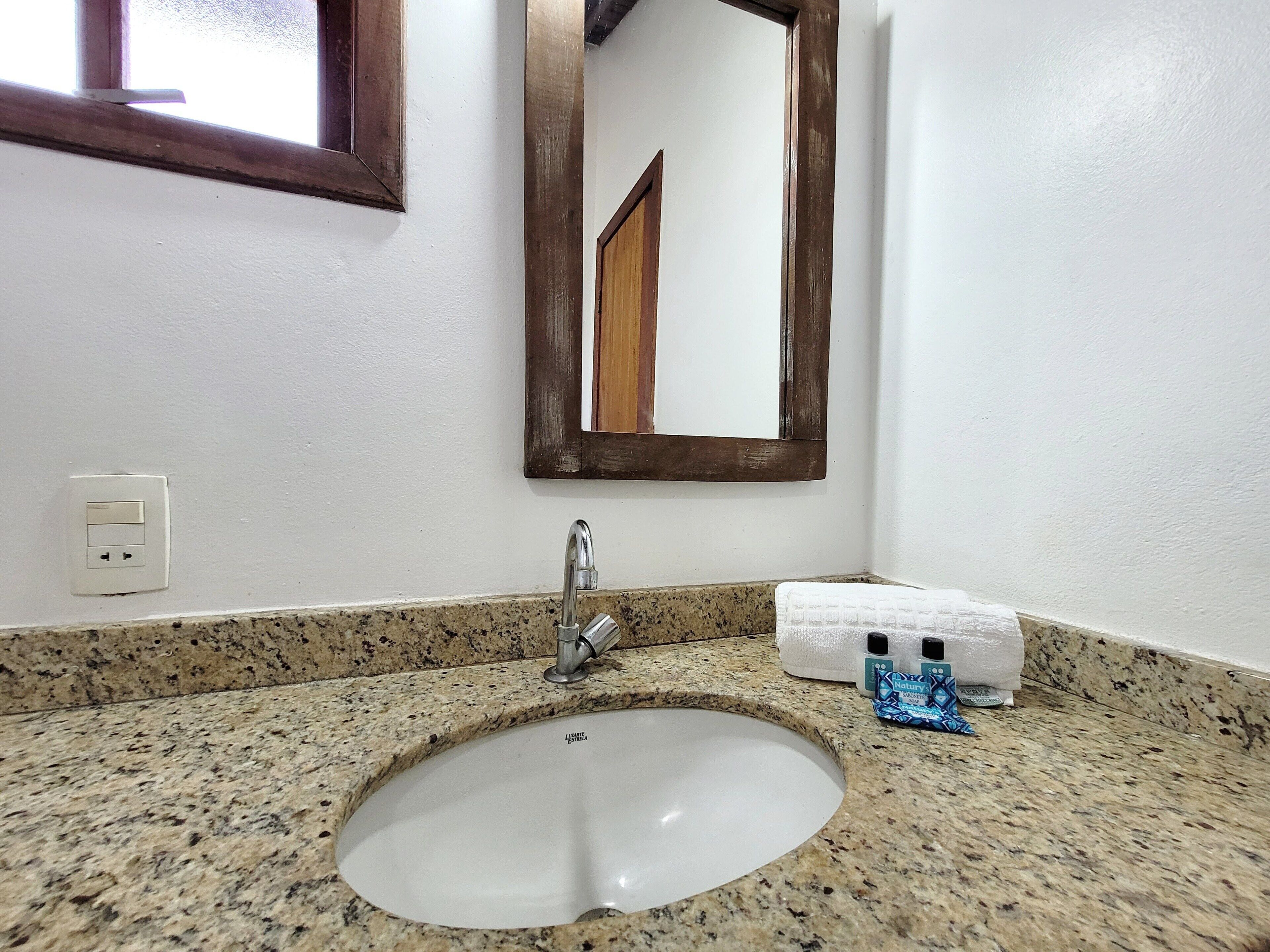 A bathroom with a granite countertop, a white sink, a mirror, and a towel dispenser.