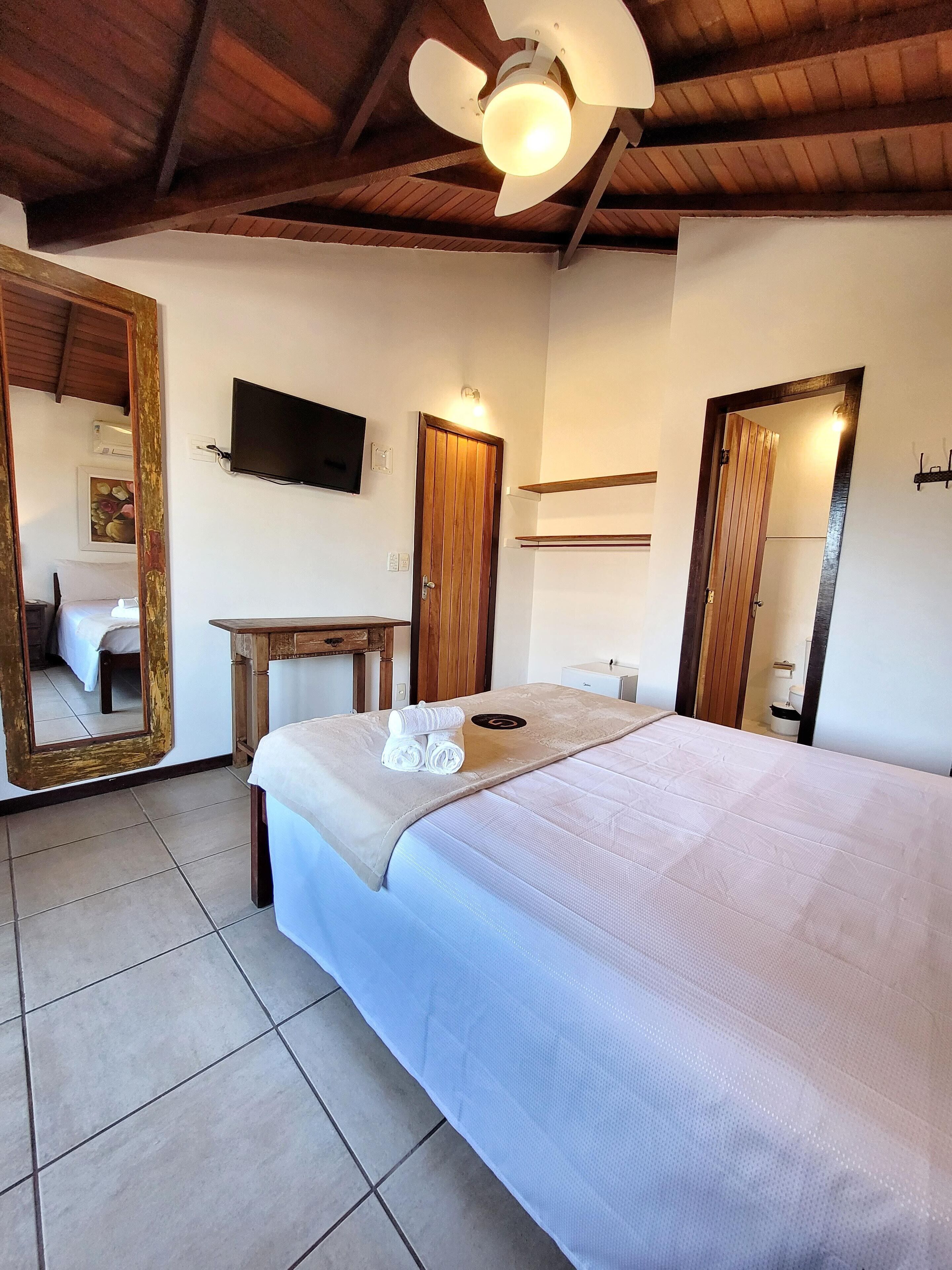 A bedroom with a large bed, a wooden ceiling, a television, and a mirror.