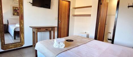 A bedroom with a large bed, a wooden ceiling, a television, and a mirror.