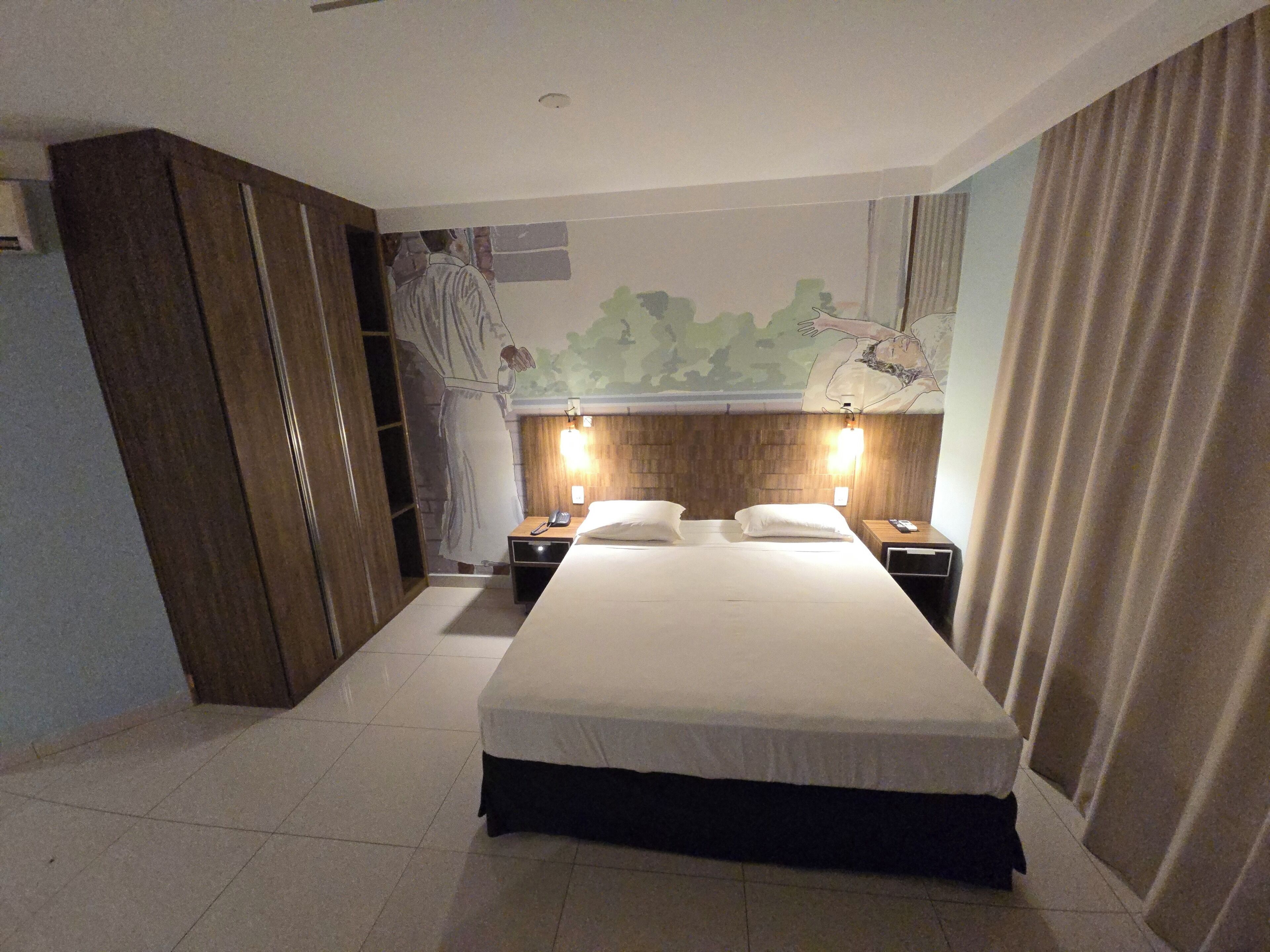 A hotel room with a large bed, wooden wardrobe, and a mural on the wall.