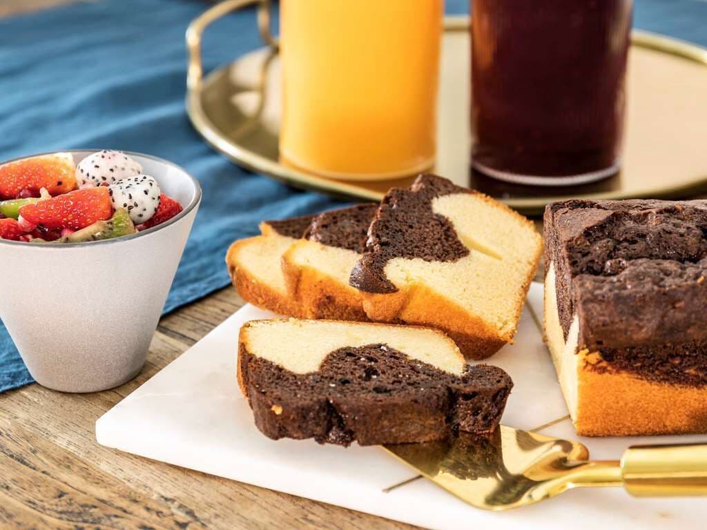 Una bandeja de postres con rebanadas de pastel de chocolate, ensalada de frutas y dos bebidas.