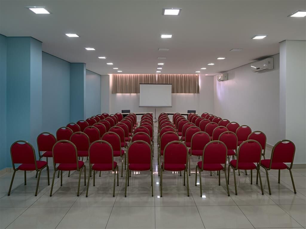 A conference room with rows of red chairs, a projector screen, and a whiteboard.