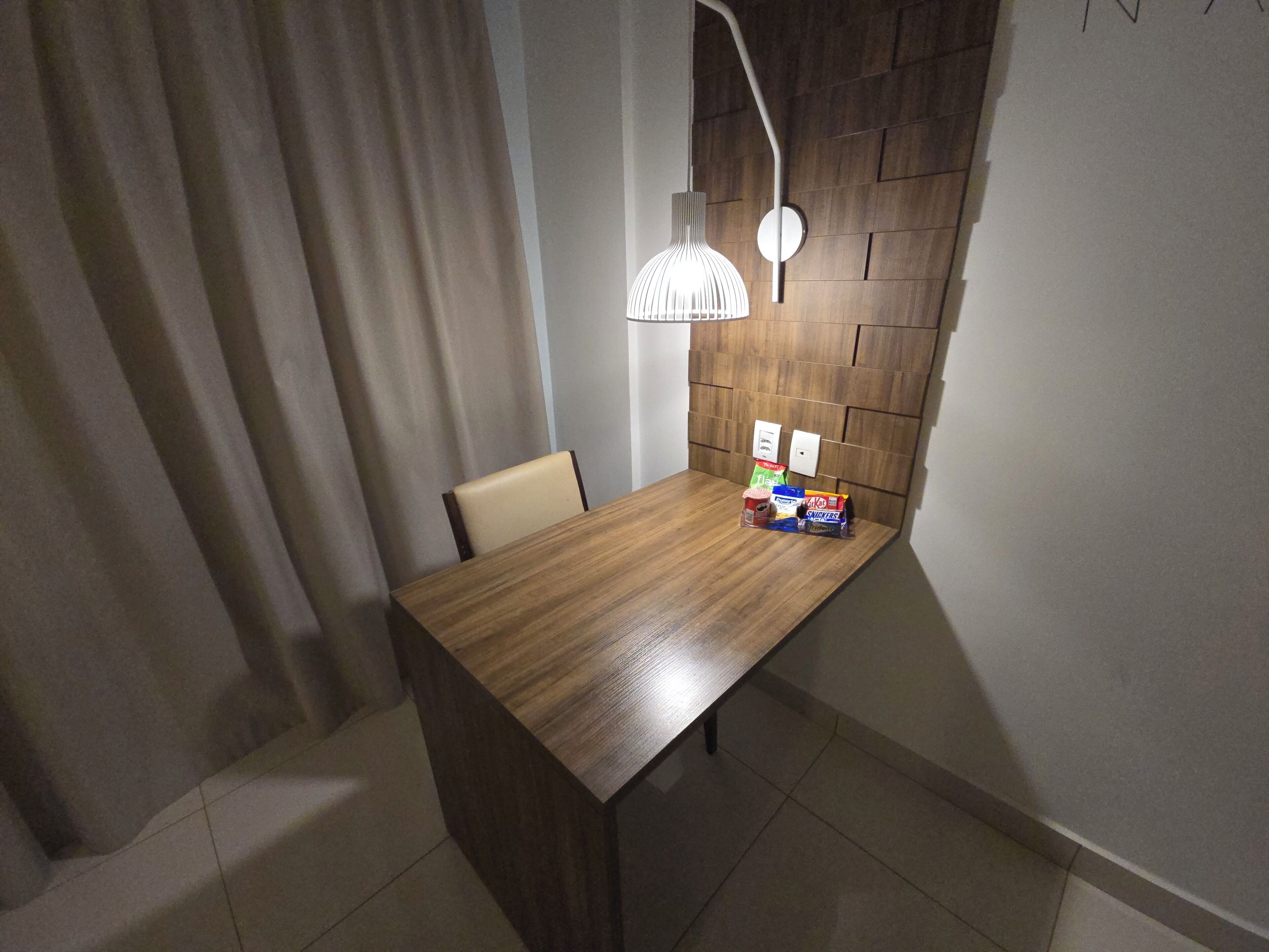 A wooden dining table with a modern pendant light, a chair, and a small selection of snacks.