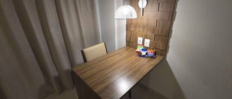 A wooden dining table with a modern pendant light, a chair, and a small selection of snacks.
