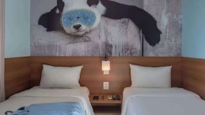 A hotel room with two beds, a wooden headboard, a nightstand with a lamp, and a wall mural of a panda.