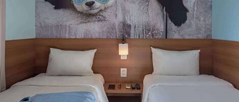 A hotel room with two beds, a wooden headboard, a nightstand with a lamp, and a wall mural of a panda.