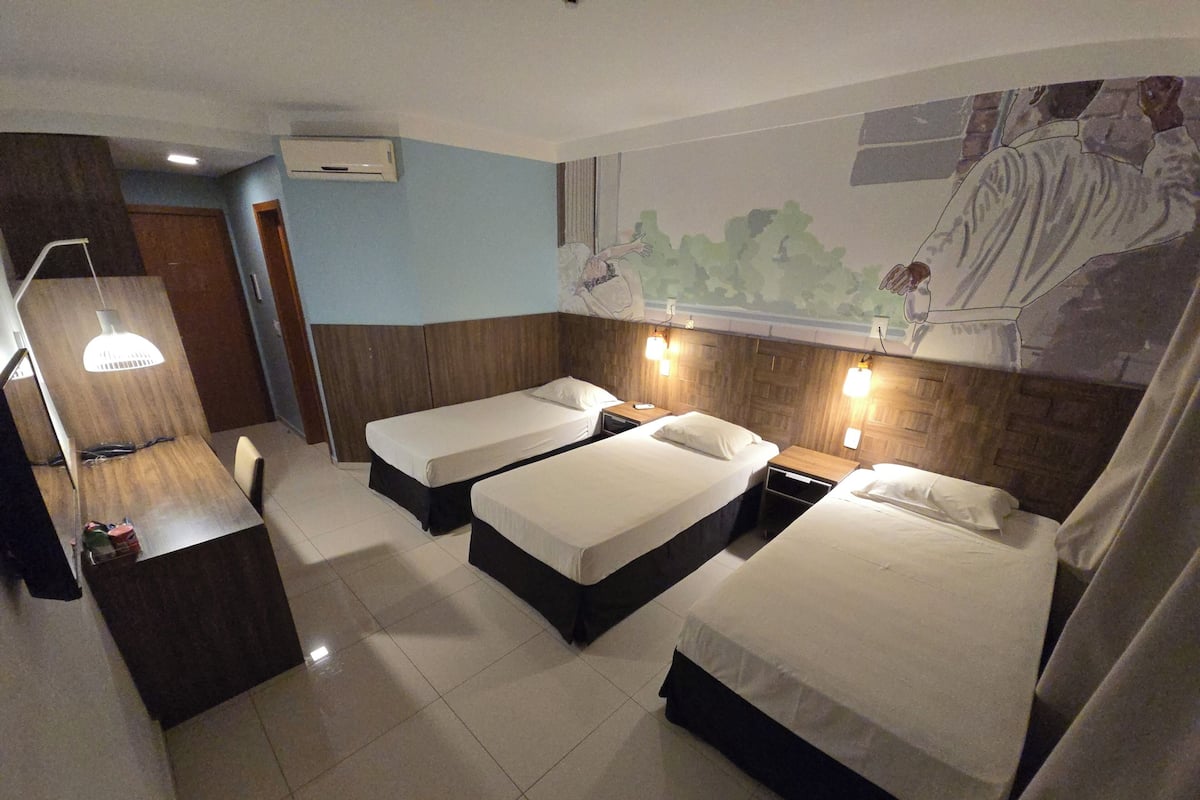 A hotel room with two single beds, a desk with a lamp, and a mural on the wall.