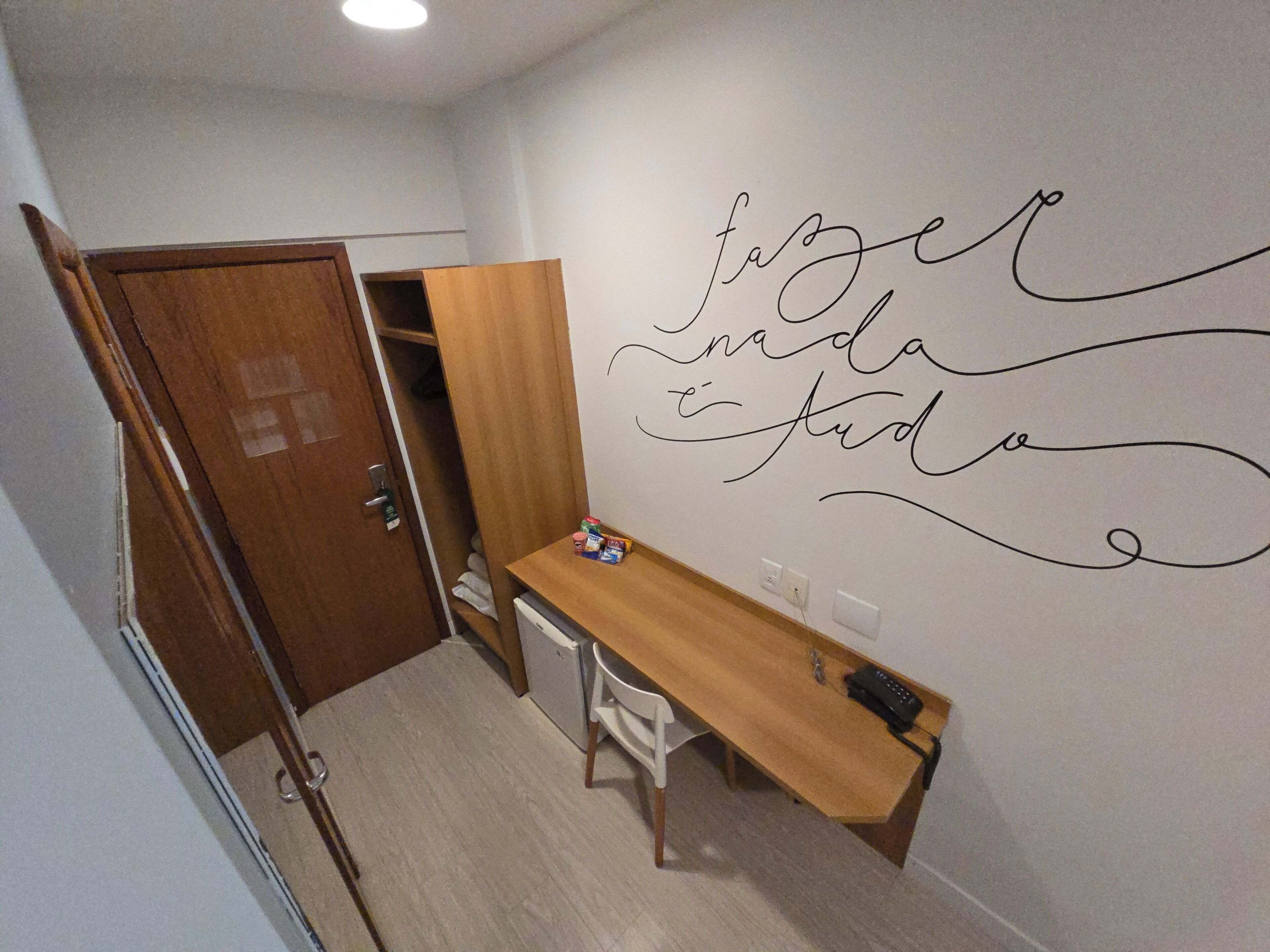 A small room with a wooden desk, a chair, and a wardrobe. There is a wall with a decorative phrase written on it.