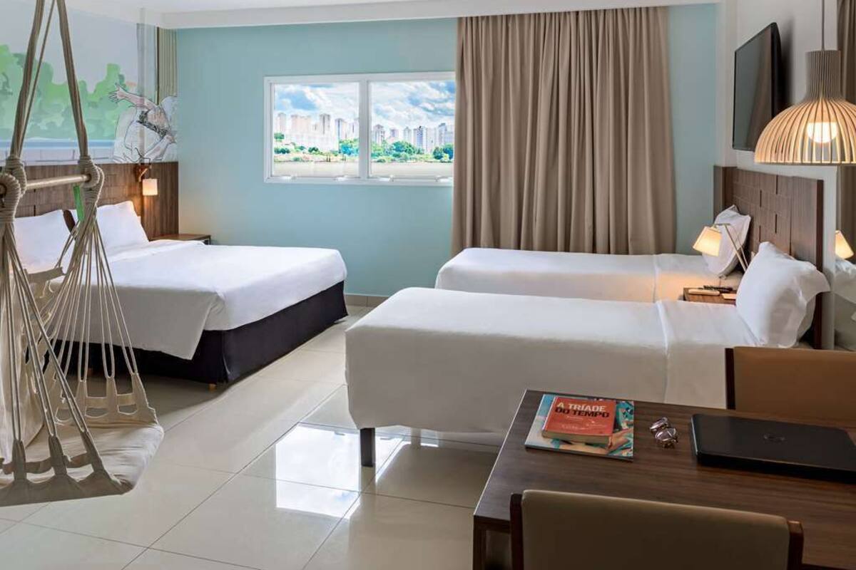 A hotel room with two beds, a sofa, a dining table, and a hanging chair.