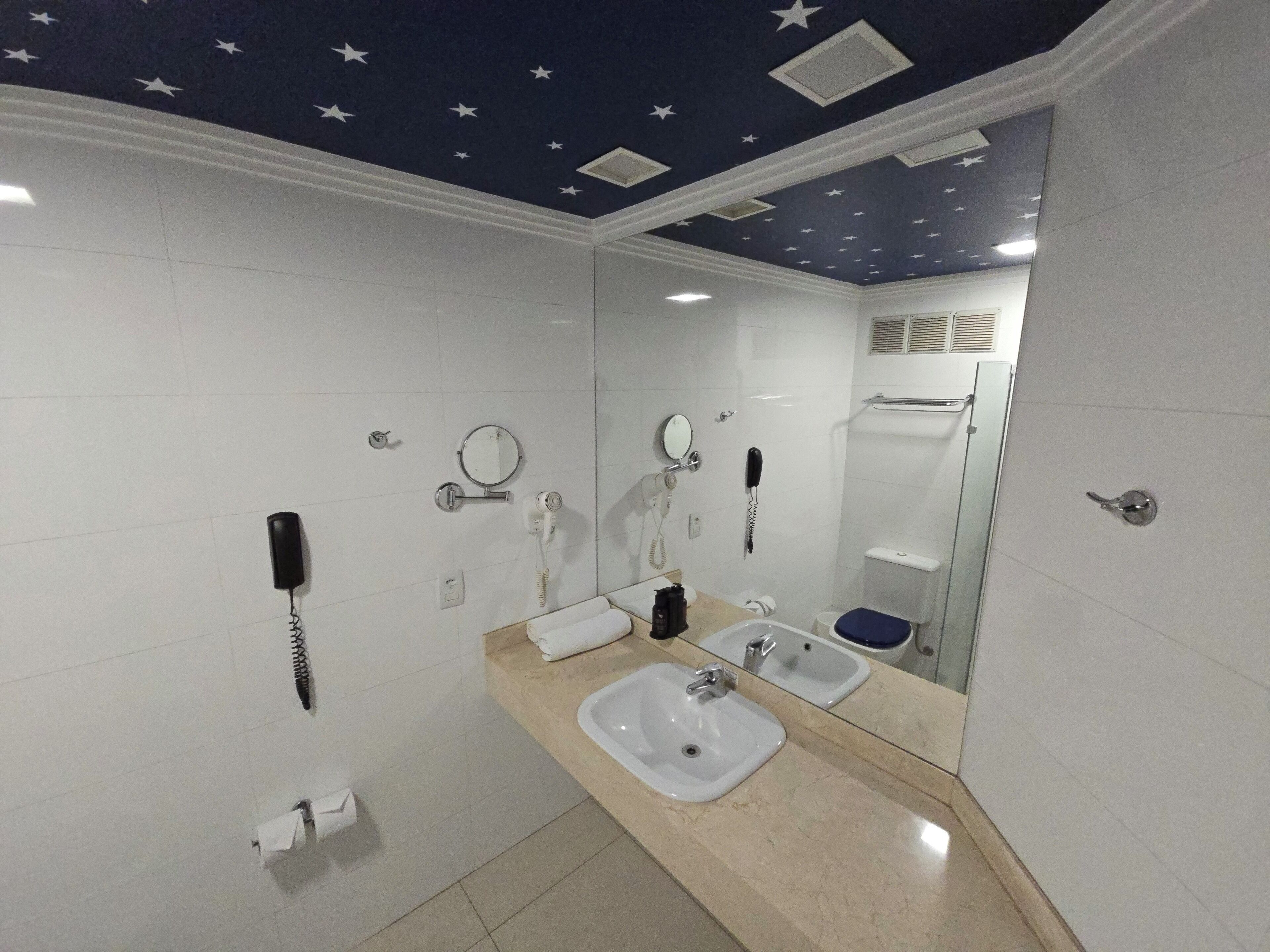 A bathroom with a star-patterned ceiling, a sink, a mirror, a telephone, and a towel rack.