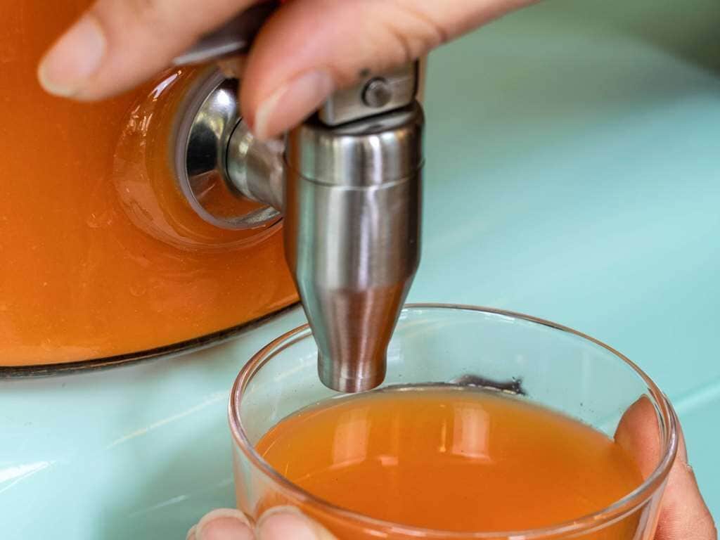 A hand pouring tea from a metallic kettle into a clear glass.