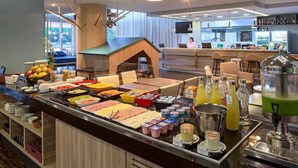 A buffet with various food items and beverages, a seating area with a counter, and a bar area with a television.