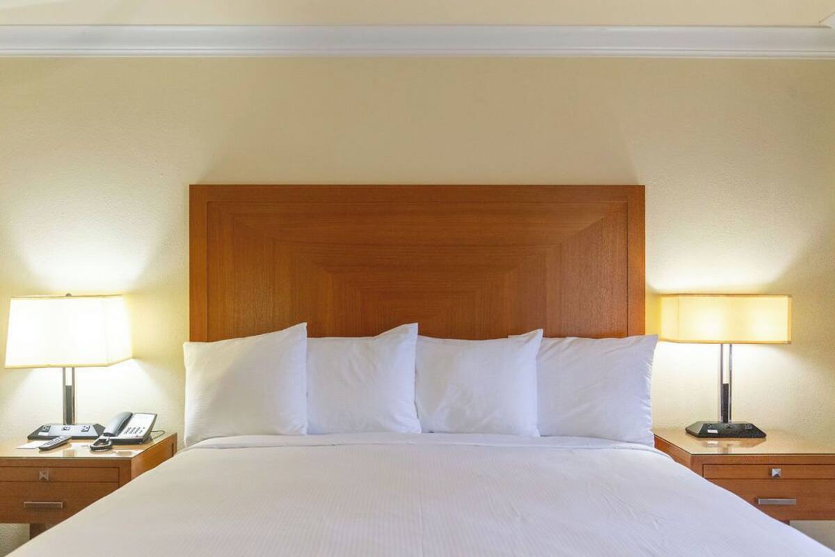 Una habitación de hotel con una cama grande, dos mesitas de noche con lámparas y un cabecero de madera.