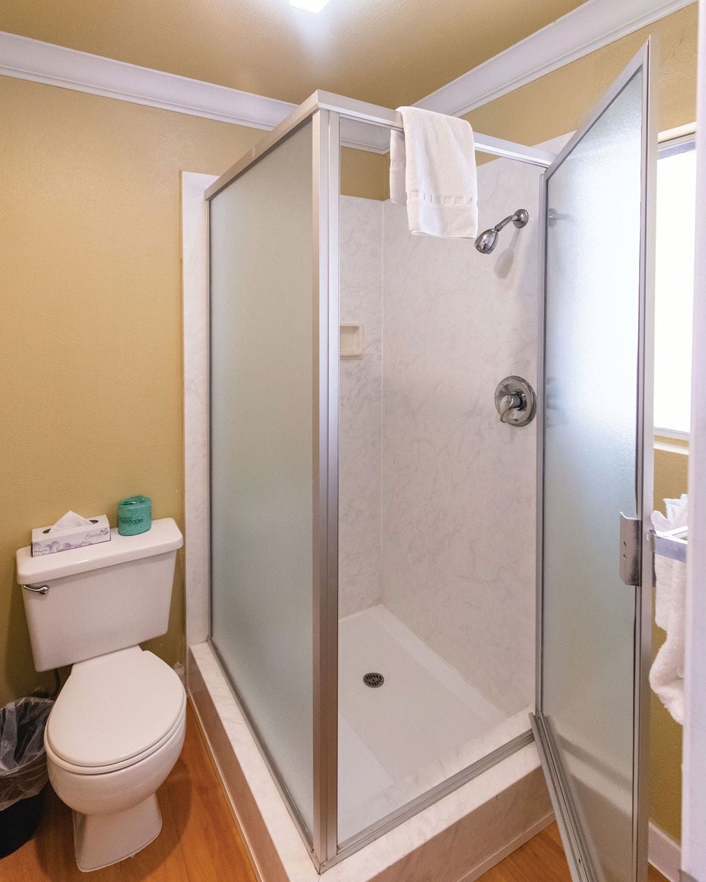 Cabina de ducha con puerta de vidrio, inodoro y toalla colgada en la puerta.